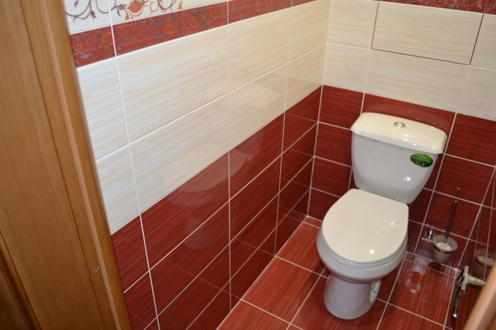 Красно-бежевый туалет с узорами на плитке и скрытым шкафом