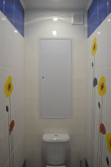 Светлый маленький туалет с цветами на плитке и металлической дверцей сантехшкафа