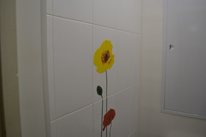Светлый маленький туалет с цветами на плитке и металлической дверцей сантехшкафа