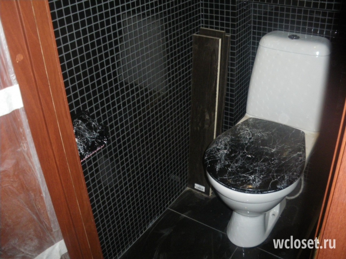 Туалет с черной плиткой под мозайку и унитазом с черной крышкой с узорами